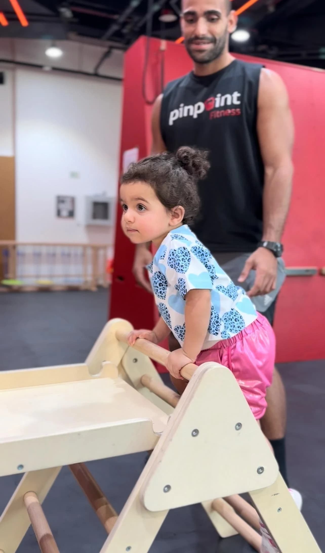 A toddler climbing an obstacle course station while a coach supports her at Pinpoint Fitness